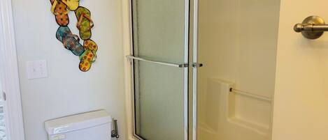A bathroom with a toilet, a shower with a glass door, and a wall decoration.