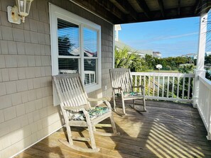 A wooden deck with two rocking chairs, a white railing, and a window with blinds.
