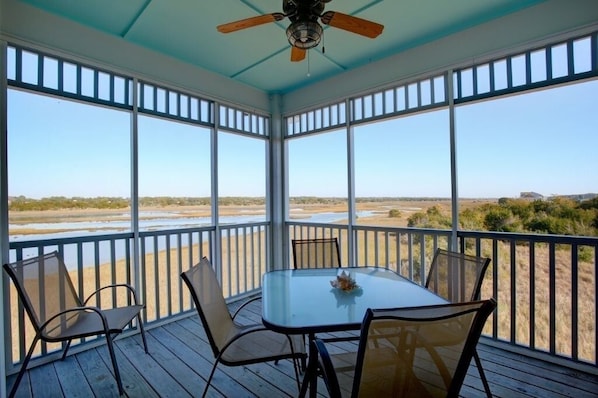 A covered outdoor area with a table and chairs, large windows, and a ceiling fan.
