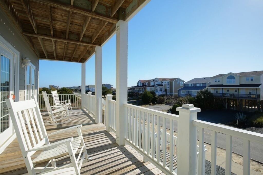 A wooden deck with white railings and chairs, overlooking a residential area with houses.