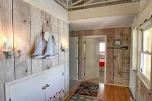 A hallway with wooden walls, a white door, and a red bed in the background. - Carolina Moon 4 Bedroom Home by RedAwning (Supply)