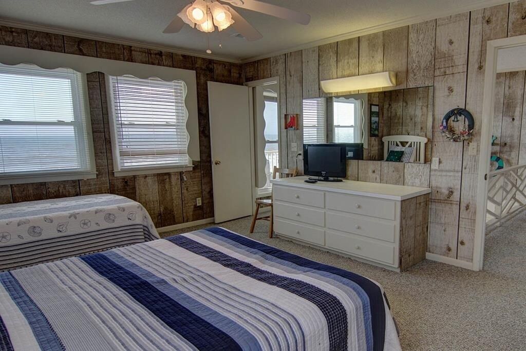 Ein Schlafzimmer mit Bett, Kommode, Fernseher und Holzwänden.
