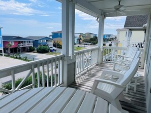 A covered porch with white chairs, a ceiling fan, and a view of colorful houses in the background. - Carpe Diem 4 Bedroom Home by RedAwning (Supply)