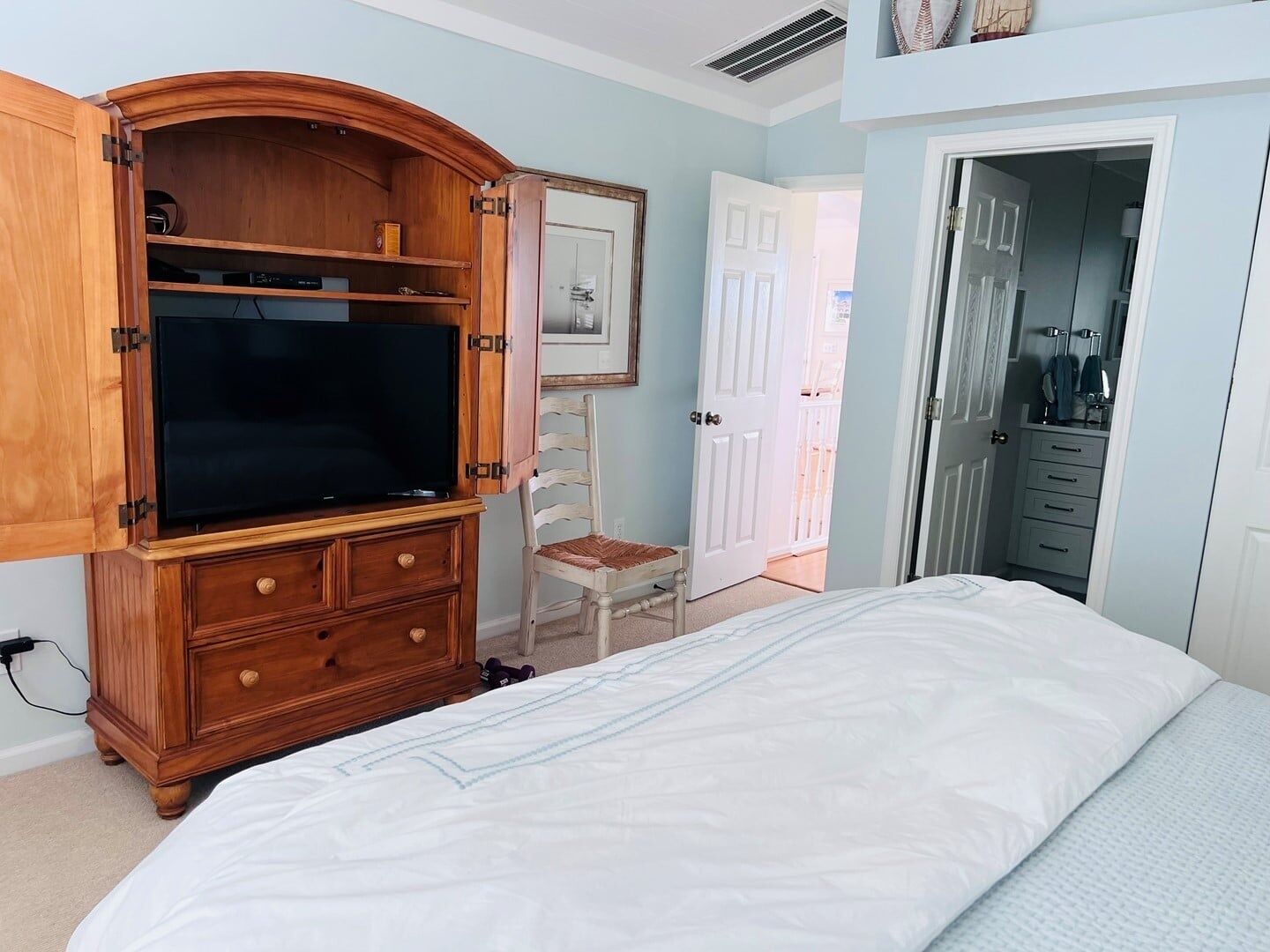 A bedroom with a bed, wooden dresser, and a television.