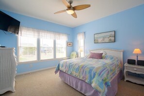 A bedroom with a bed, a ceiling fan, a TV, a window with blinds, and a chair.