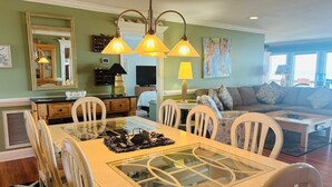 A dining area with a glass-top table, white chairs, and pendant lighting.