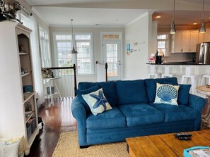 A living room with a blue sofa, a wooden coffee table, and a kitchen area with white cabinets and stainless steel appliances. - Compass Rose 4 Bedroom Home by RedAwning (Supply)