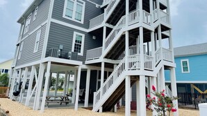 Una casa de varios pisos con un porche cubierto, mobiliario exterior y una escalera que conduce a un balcón.