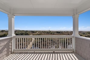 A covered balcony with a view of a beach and dry vegetation. - Cypress Hall 6 Bedroom Home by RedAwning (Supply)