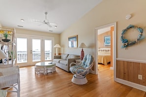A spacious living room with a ceiling fan, a sofa, a chair, a small table, and a balcony door. - Cypress Hall 6 Bedroom Home by RedAwning (Supply)