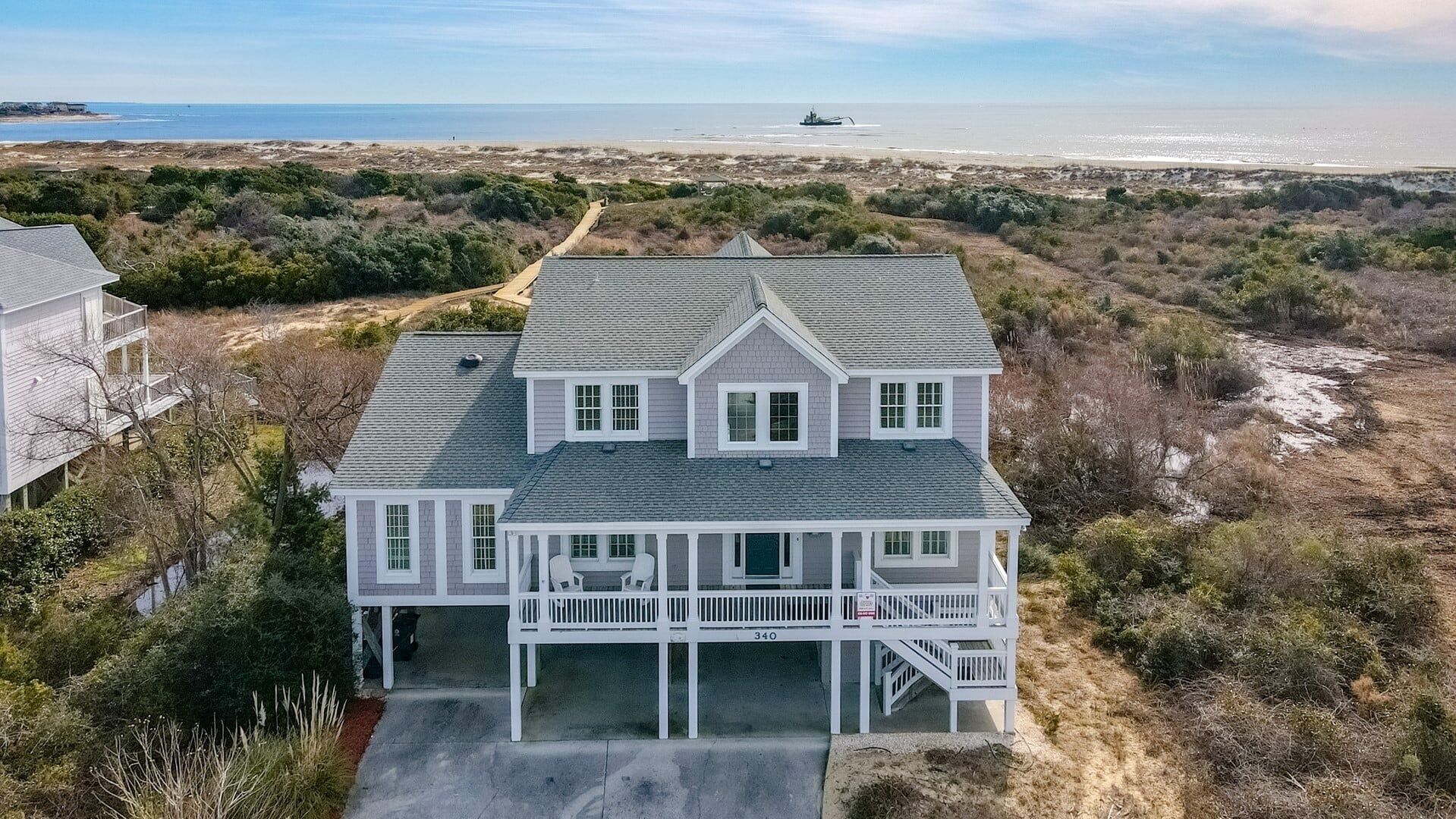 A two-story house with a covered porch and a view of the beach and ocean.