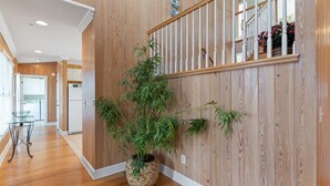 Un couloir aux murs lambrissés, un escalier et une grande plante en pot.