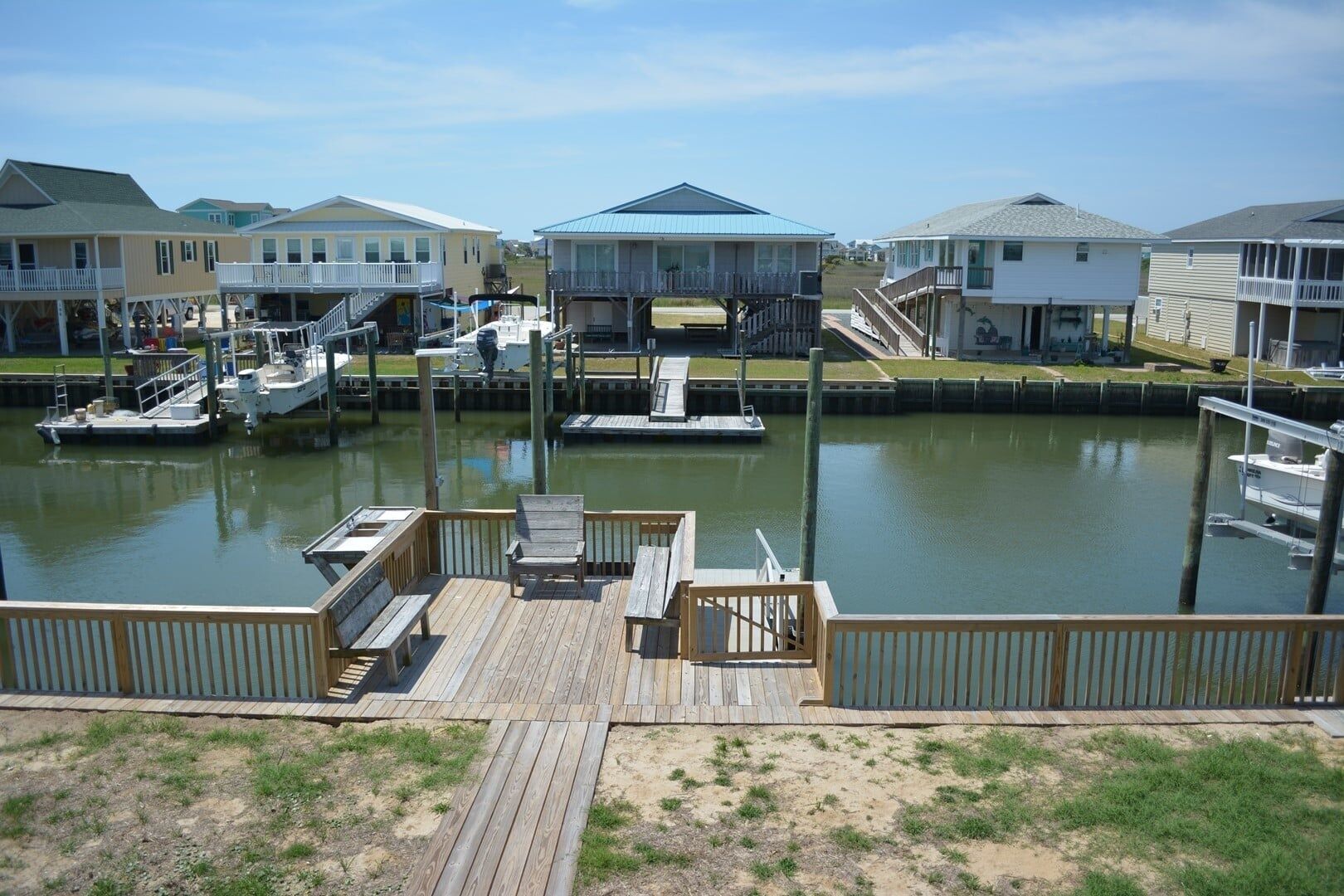Un puerto deportivo con barcos amarrados, una terraza de madera con asientos y casas con balcones.