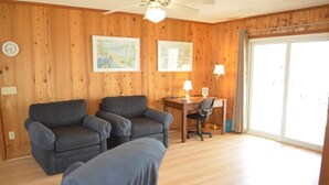 A room with wooden walls, a desk with a chair, two armchairs, a lamp, and a window. - Do-little Dock 3 Bedroom Home by RedAwning (Supply)