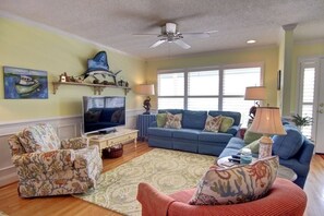 A living room with a television, two sofas, a patterned rug, and decorative items on shelves. - Turtle Cove (formerly Fiddler's Green) 4 Bedroom Home by RedAwning (Supply)