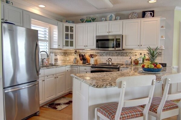 A kitchen with white cabinets, stainless steel appliances, a granite countertop, and a fruit bowl. - Turtle Cove (formerly Fiddler's Green) 4 Bedroom Home by RedAwning (Supply)