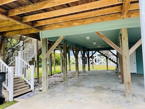 A covered outdoor area with wooden beams, a concrete floor, and a white staircase.