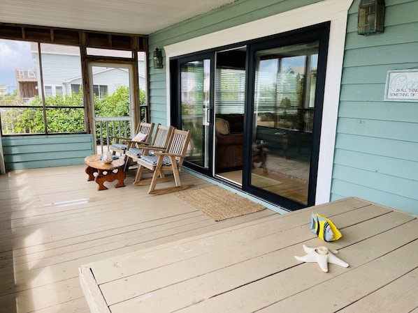 Une véranda couverte avec des meubles en bois, une porte-fenêtre coulissante et une vue sur le jardin arrière.