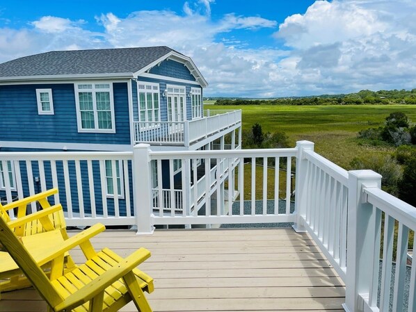 Une maison à deux étages avec un balcon, une terrasse en bois et une vue sur un champ verdoyant.