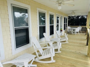 A covered porch with white rocking chairs and a table, large windows, and ceiling fans. - Dry Dock - 4 Br Home (Supply)