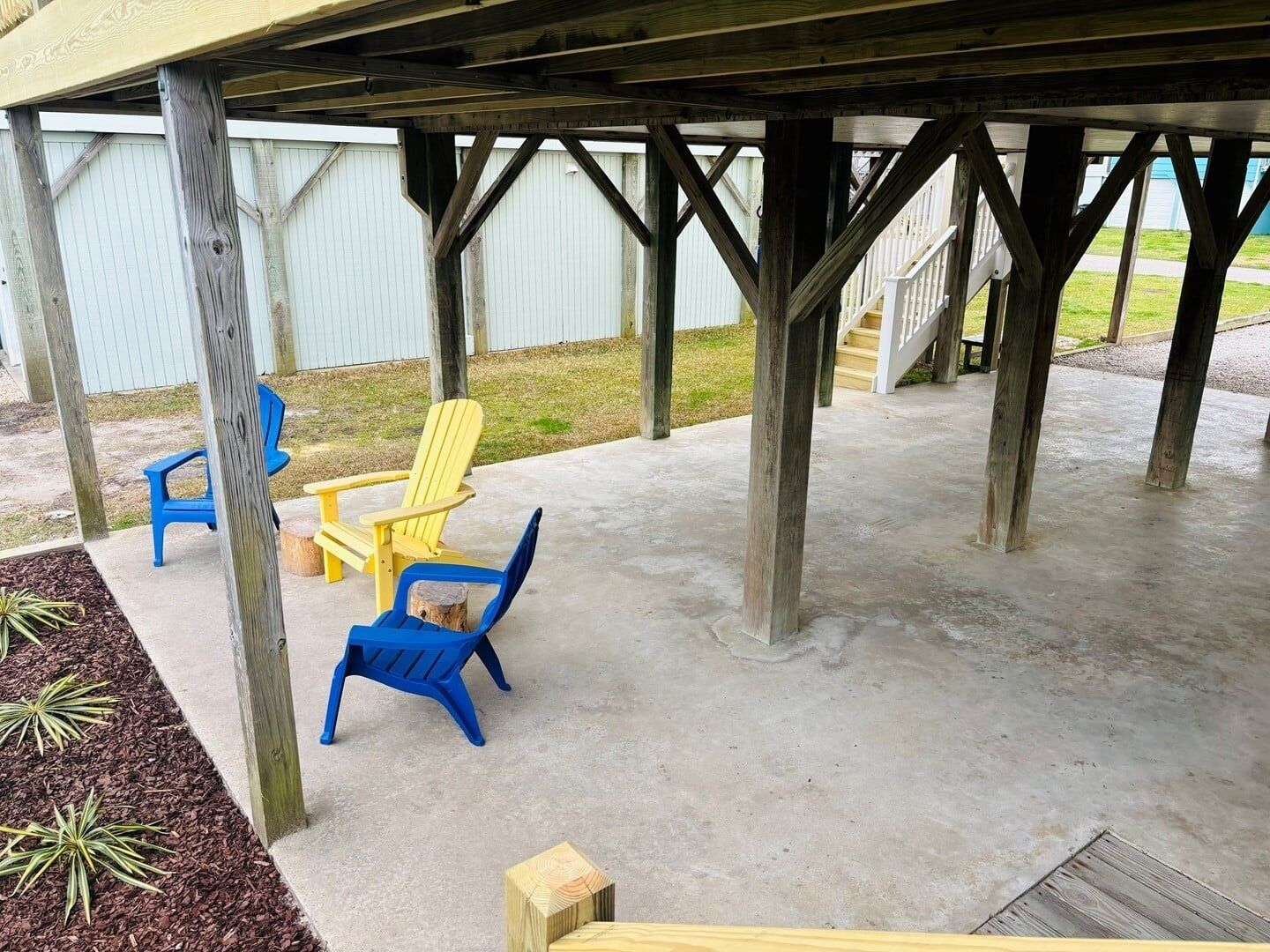 Een overdekte zitruimte met houten palen, een betonnen vloer en twee stoelen.