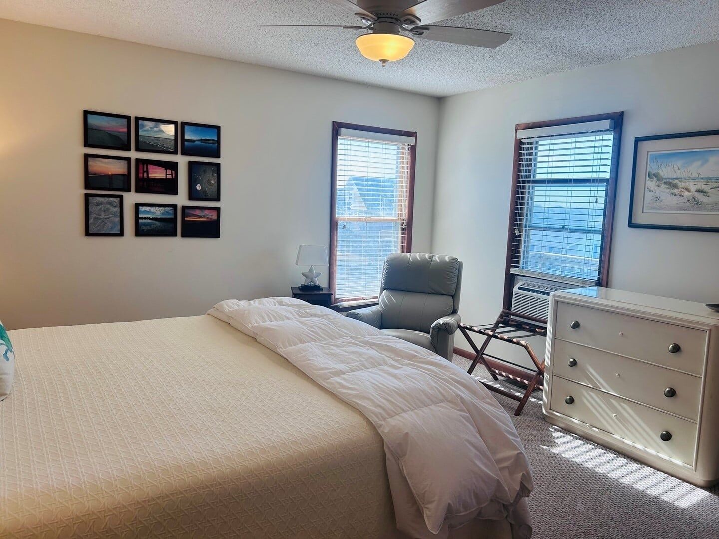 Een slaapkamer met een bed, een stoel, een dressoir en een plafondventilator.
