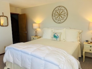 A neatly made bed with a white comforter and pillows, a decorative wall piece, and bedside lamps on nightstands.