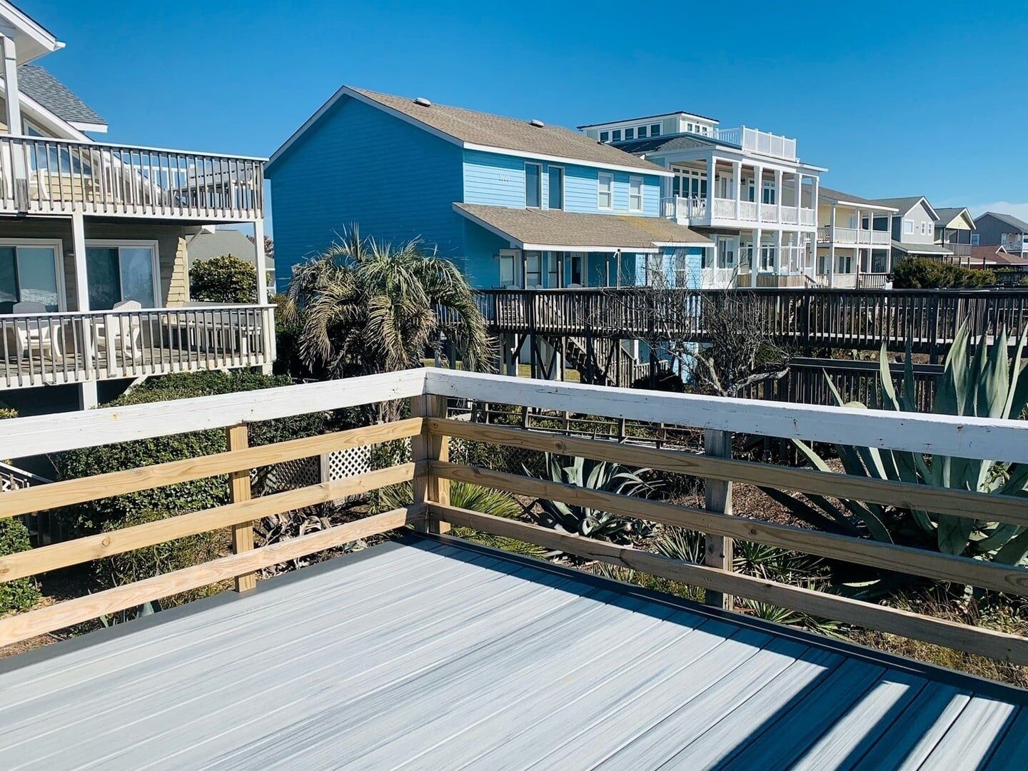 A wooden deck with a railing, a blue building, and a white building in the background.