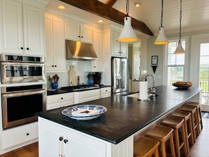 A modern kitchen with white cabinetry, stainless steel appliances, a black countertop, and wooden bar stools. - Gray Goose 5 Bedroom Home by RedAwning (Supply)