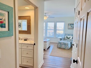 A hallway leading to a bedroom with a bed, a dresser, and a window with blinds. - Dune Escape 5 Bedroom Home by RedAwning (Supply)