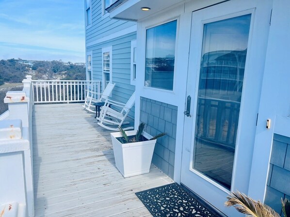 A balcony with white railings, a door, and two rocking chairs.