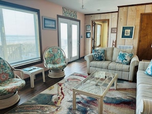 A living room with a sofa, armchair, and coffee table, wooden panel walls, and framed pictures.