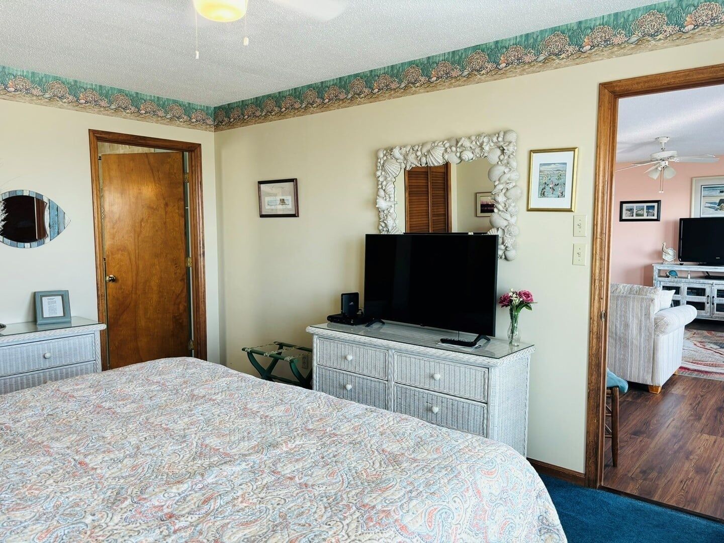A bedroom with a large bed, a dresser with a flat-screen TV, a mirror, and a door leading to another room.