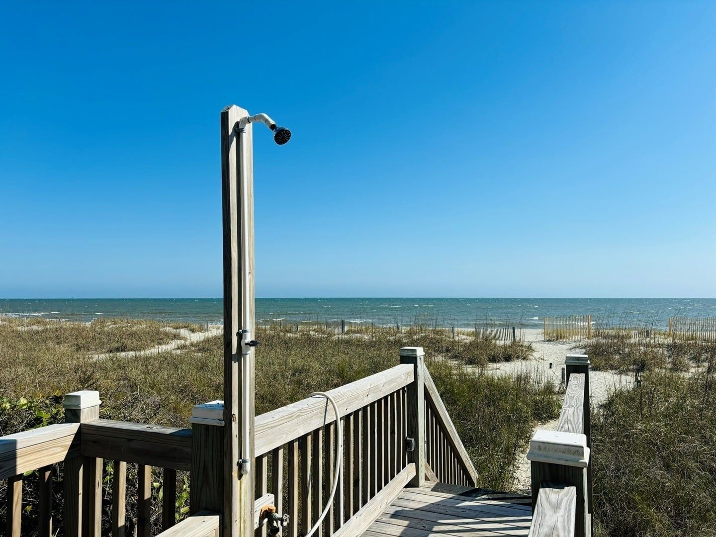 A wooden boardwalk leading to a beach with a clear view of the ocean.