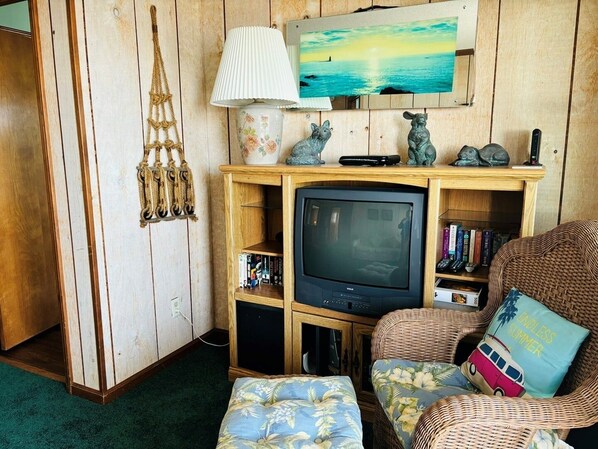 A living room with a television, books, a lamp, and a wall-mounted painting.