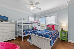 Een slaapkamer met stapelbedden, een dressoir, een nachtkastje groen en een plafondventilator.