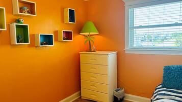 Relax in this cozy space with a blue and white striped bed against a vibrant wall, a dresser with multiple drawers, and a lamp.