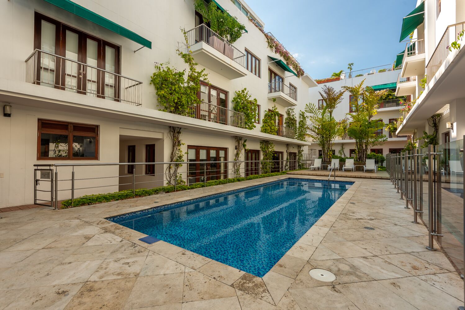 A modern building with a swimming pool, balconies with plants, and a clear sky.