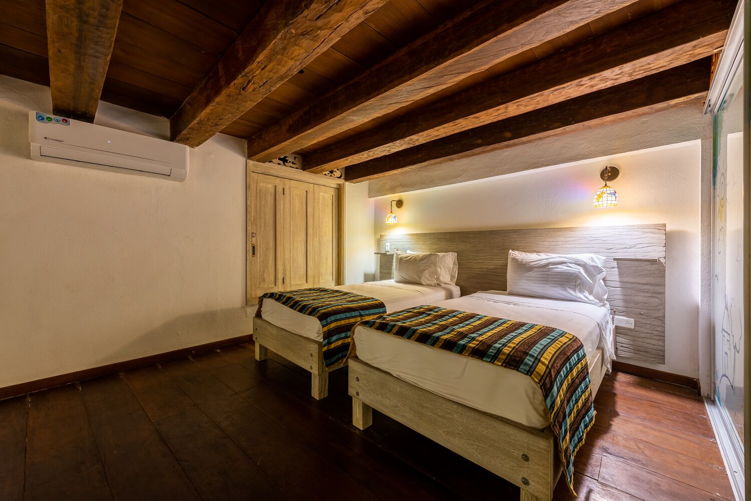 A bedroom with two beds, wooden beams, a wardrobe, and a wall-mounted air conditioner.