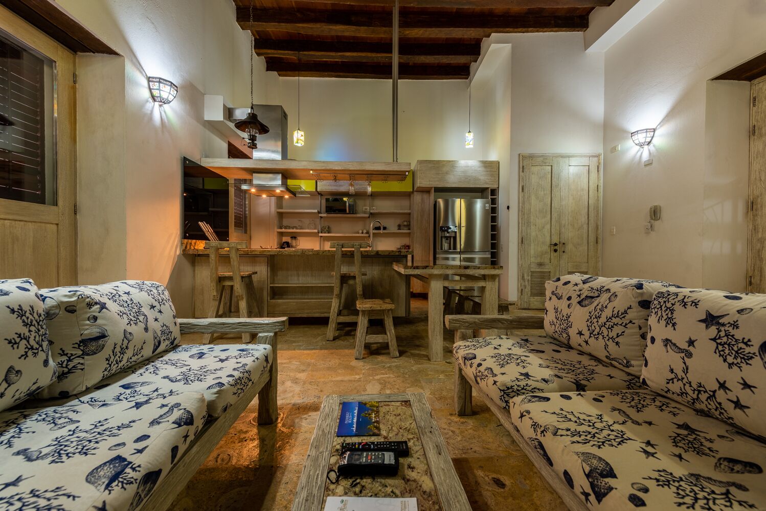 A cozy living room with two patterned sofas, a coffee table, and a kitchen area with a refrigerator and microwave.
