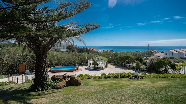 Zona de piscina con un pequeño jardín, una pérgola y vistas al mar.