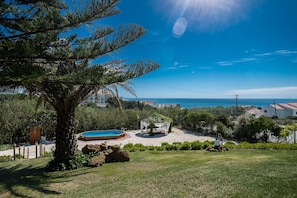 A pool area with a small garden, a pergola, and a view of the sea. - Ericeira Villa Surf Camp Hostel (Mafra)