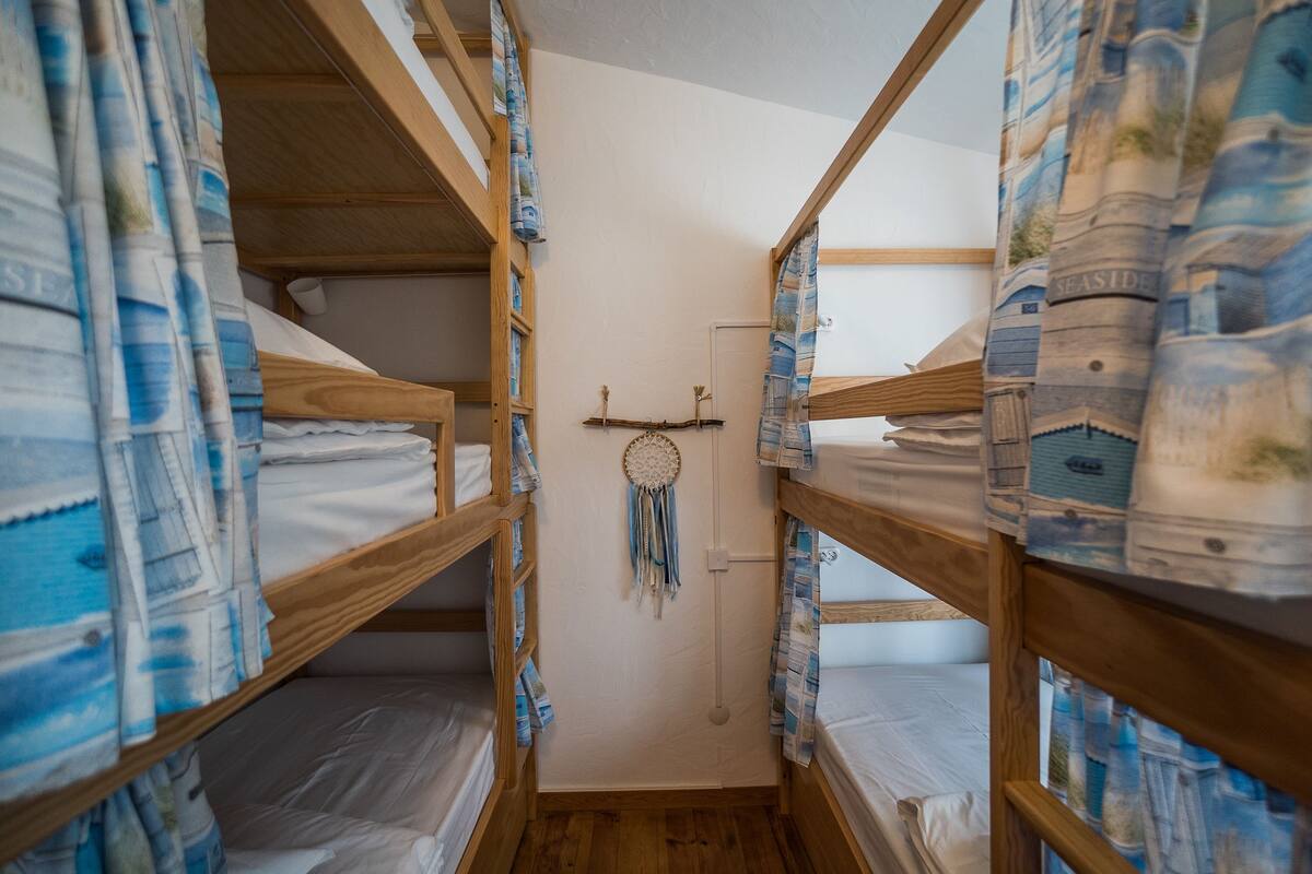 Un pasillo estrecho con literas a ambos lados, cada una cubierta con ropa de cama de diseño azul y blanco.