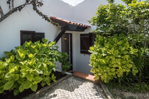 A courtyard with a white building, a tiled roof, and lush green plants. - Ericeira Villa Surf Camp Hostel (Mafra)
