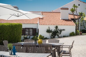 An outdoor patio with wooden tables and chairs, white umbrellas, and potted plants. - Ericeira Villa Surf Camp Hostel (Mafra)