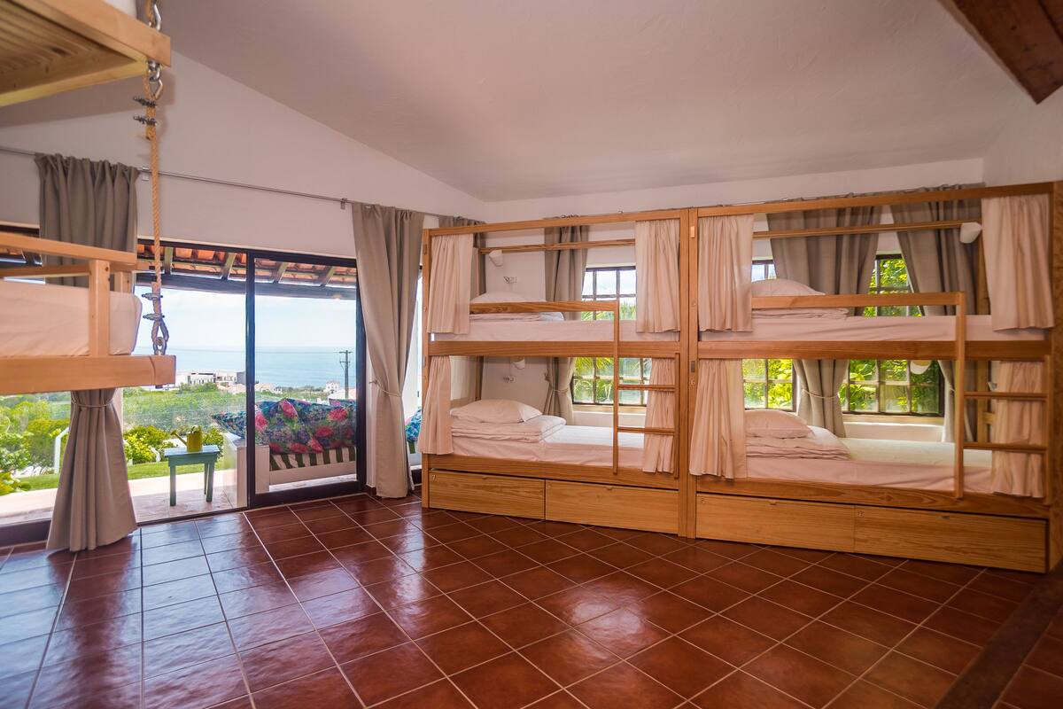 Una habitación con literas, puerta corrediza al balcón y vistas a zonas verdes y edificios.
