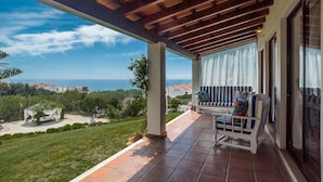 Un espacio al aire libre techado con vistas al mar, una silla blanca y un sofá a rayas.