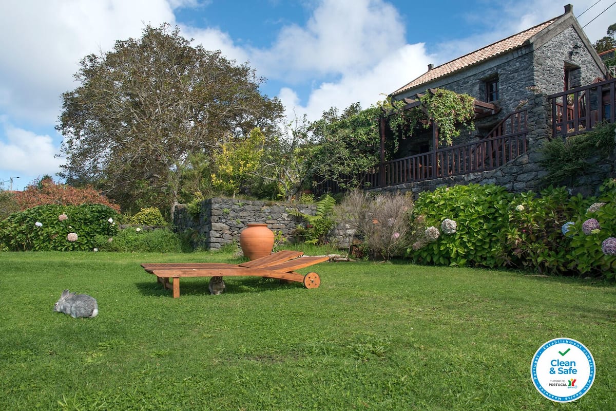 Une maison en pierre avec un jardin, une terrasse en bois et un grand pot en terre cuite.