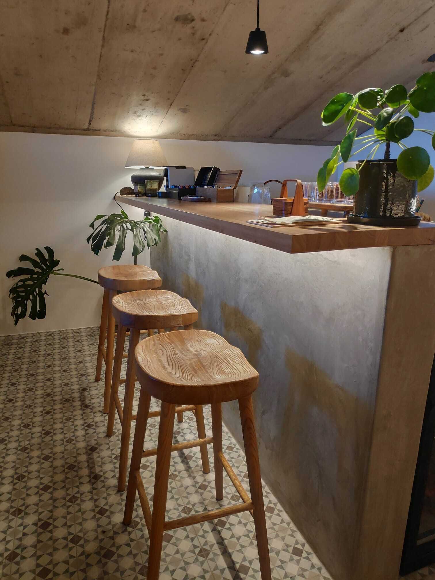 Una cocina con barra, taburetes de madera, una planta en maceta y suelo de baldosas.