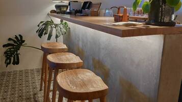 Una cocina con barra, taburetes de madera, una planta en maceta y suelo de baldosas.